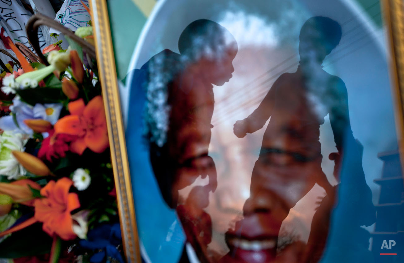  A mother, right, walks to have a family photograph taken with her son, center, seen reflected in a portrait of Nelson Mandela, outside the Mediclinic Heart Hospital where former South African President Nelson Mandela is being treated in Pretoria, So