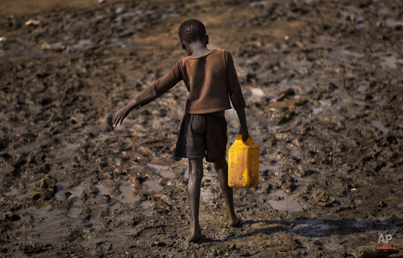  A displaced child struggles to carry a container of drinking water obtained from a truck across a slippery muddy patch of ground at a United Nations compound which has become home to thousands of people displaced by the recent fighting, in the capit