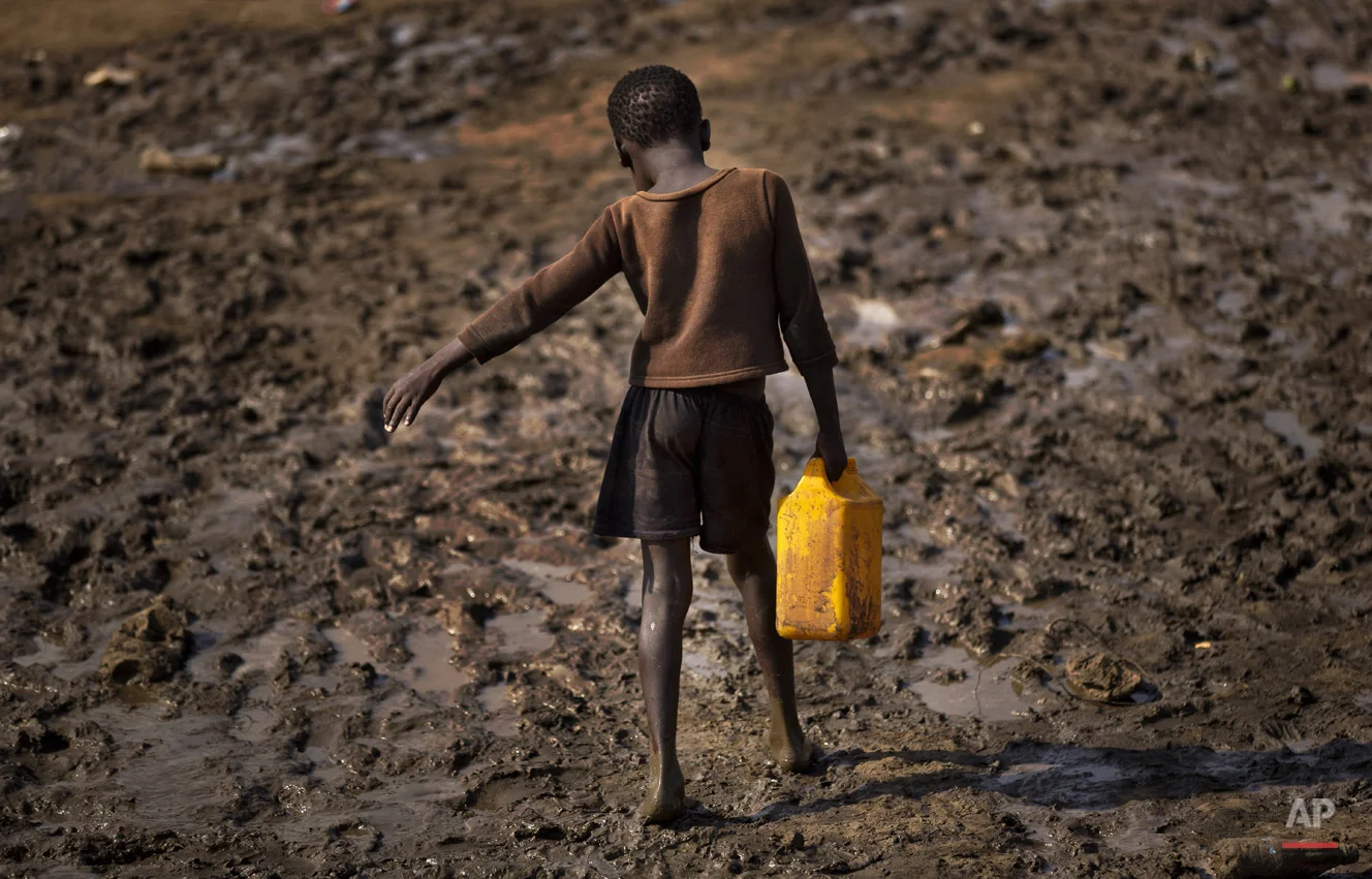 A displaced child struggles to carry a container of drinking water obtained from a truck across a slippery muddy patch of ground at a United Nations compound which has become home to thousands of people displaced by the recent fighting, in the capital Juba, South Sudan Sunday, Dec. 29, 2013. Some 25,000 people live in two hastily arranged camps for the internally displaced in Juba and nearly 40,000 are in camps elsewhere in the country, two weeks after violence broke out in the capital and a spiralling series of ethnically-based attacks coursed through the nation, killing at least 1,000 people. (AP Photo/Ben Curtis)