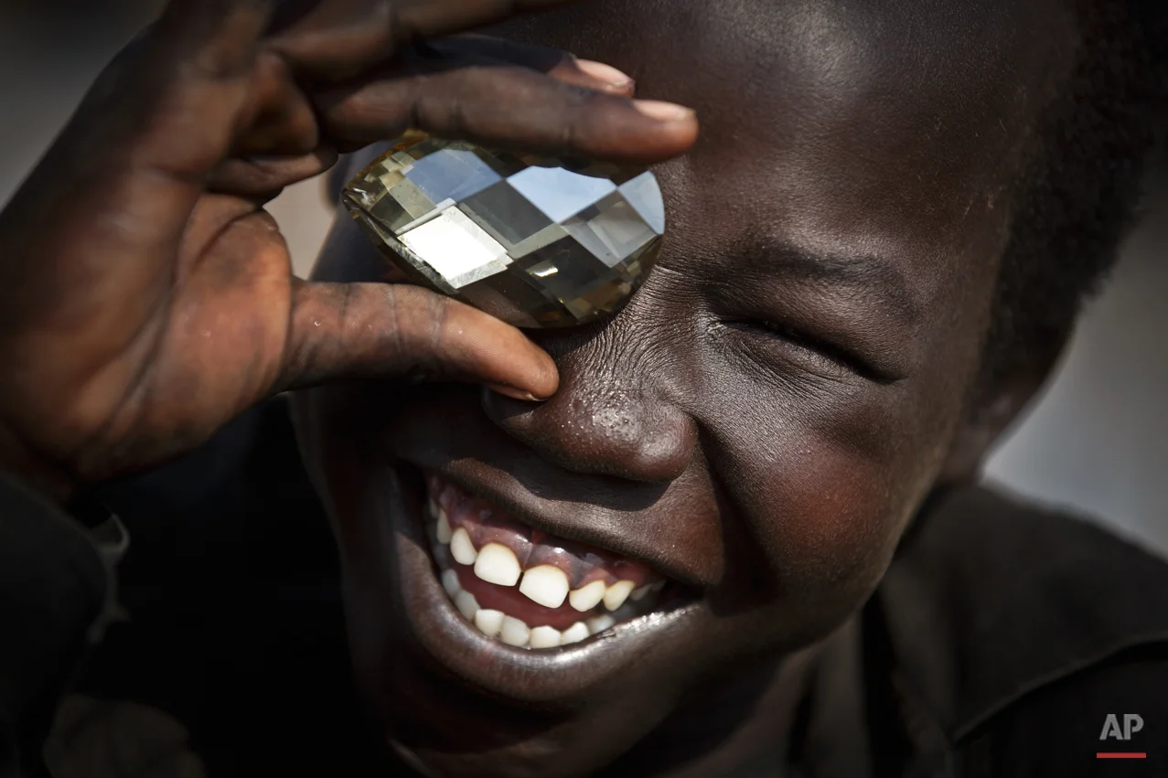 A displaced boy mimics the photographer taking a picture of him, using a fake plastic jewel, at a United Nations compound which has become home to thousands of people displaced by the recent fighting, in the capital Juba, South Sudan Sunday, Dec. 29, 2013. Some 25,000 people live in two hastily arranged camps for the internally displaced in Juba and nearly 40,000 are in camps elsewhere in the country, two weeks after violence broke out in the capital and a spiralling series of ethnically-based attacks coursed through the nation, killing at least 1,000 people. (AP Photo/Ben Curtis)