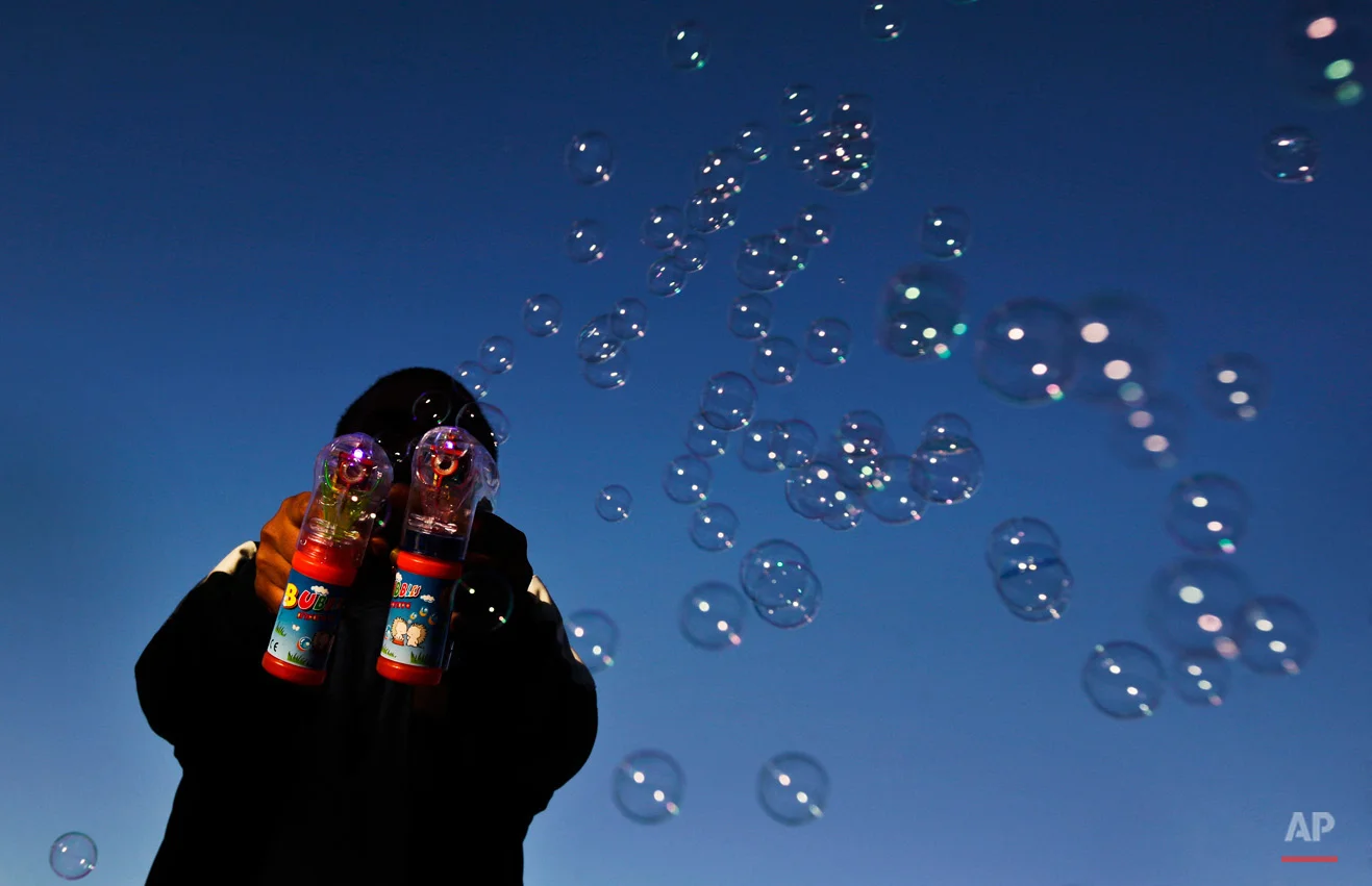 A man makes bubbles with two electric bubble-blowers at a day-long gathering of pro-Gadhafi soldiers and supporters, at dusk in Green Square, Tripoli, Libya Sunday, March 6, 2011. After unusually heavy gunfire erupted before dawn, thousands of Gadhafi's supporters poured into Tripoli's central square for a rally claimed by them to be a celebration of the regime taking back the cities of Ras Lanouf and Misrata - though both places remained in rebel hands late Sunday afternoon. (AP Photo/Ben Curtis)