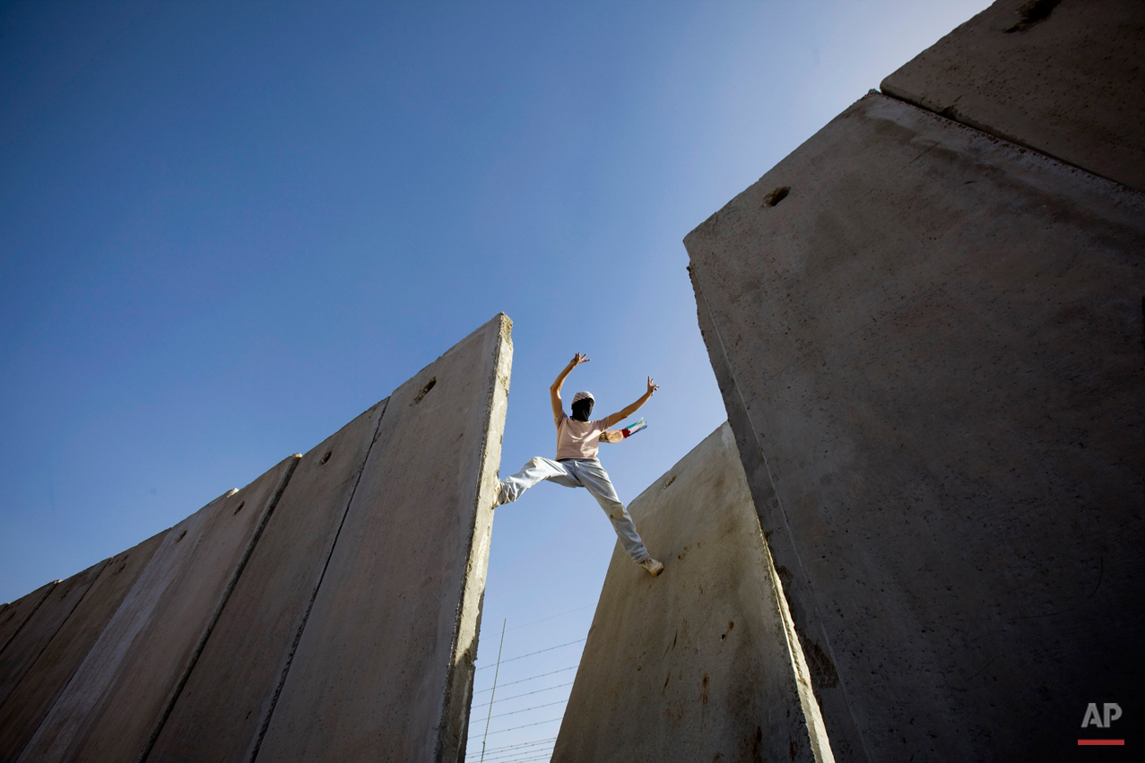  A Palestinian demonstrator gestures atop the separation barrier, moments after knocking down a segment of the concrete wall, during a protest against the barrier in the West Bank village of Nilin, near Ramallah, Friday, Nov. 6, 2009. Palestinian Pre
