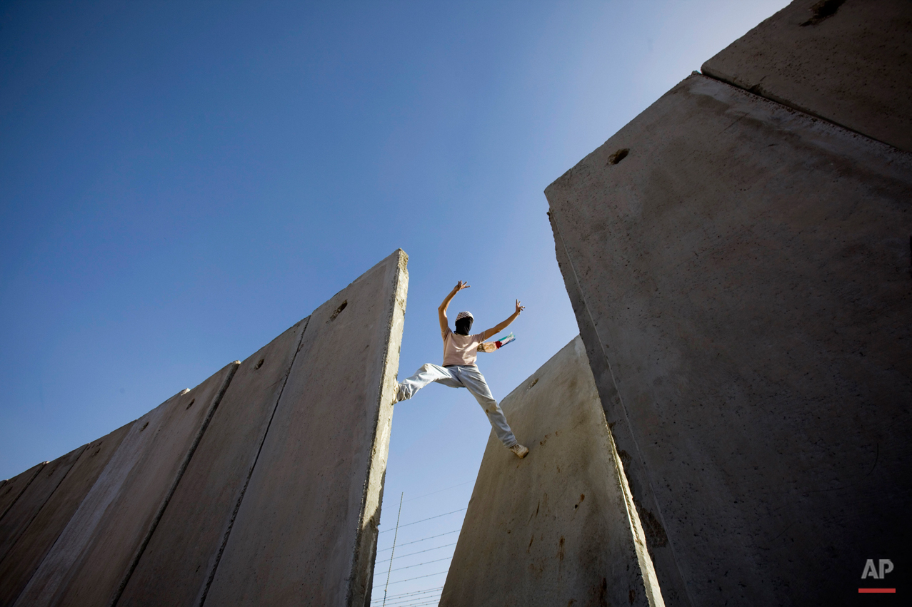 A Palestinian demonstrator gestures atop the separation barrier, moments after knocking down a segment of the concrete wall, during a protest against the barrier in the West Bank village of Nilin, near Ramallah, Friday, Nov. 6, 2009. Palestinian President Mahmoud Abbas said Thursday he does not want to run for another term in the January elections, blaming a stalemate in Mideast peace talks on Israel and the United States. (AP Photo/Bernat Armangue)