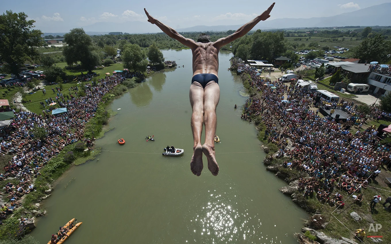 Spectators watch as a diver Sali Riza Grancina, winner of the competition, performs the winning jump from the Ura e Shenjte bridge during the traditional annual high diving competition, near the town of Gjakova, 100 kms south of Kosovo capital Pristina on Sunday, Aug. 10, 2014. Total of 27 divers from Kosovo competed diving 22 meters high bridge into the Drini i Bardhe river. (AP Photo/Visar Kryeziu)