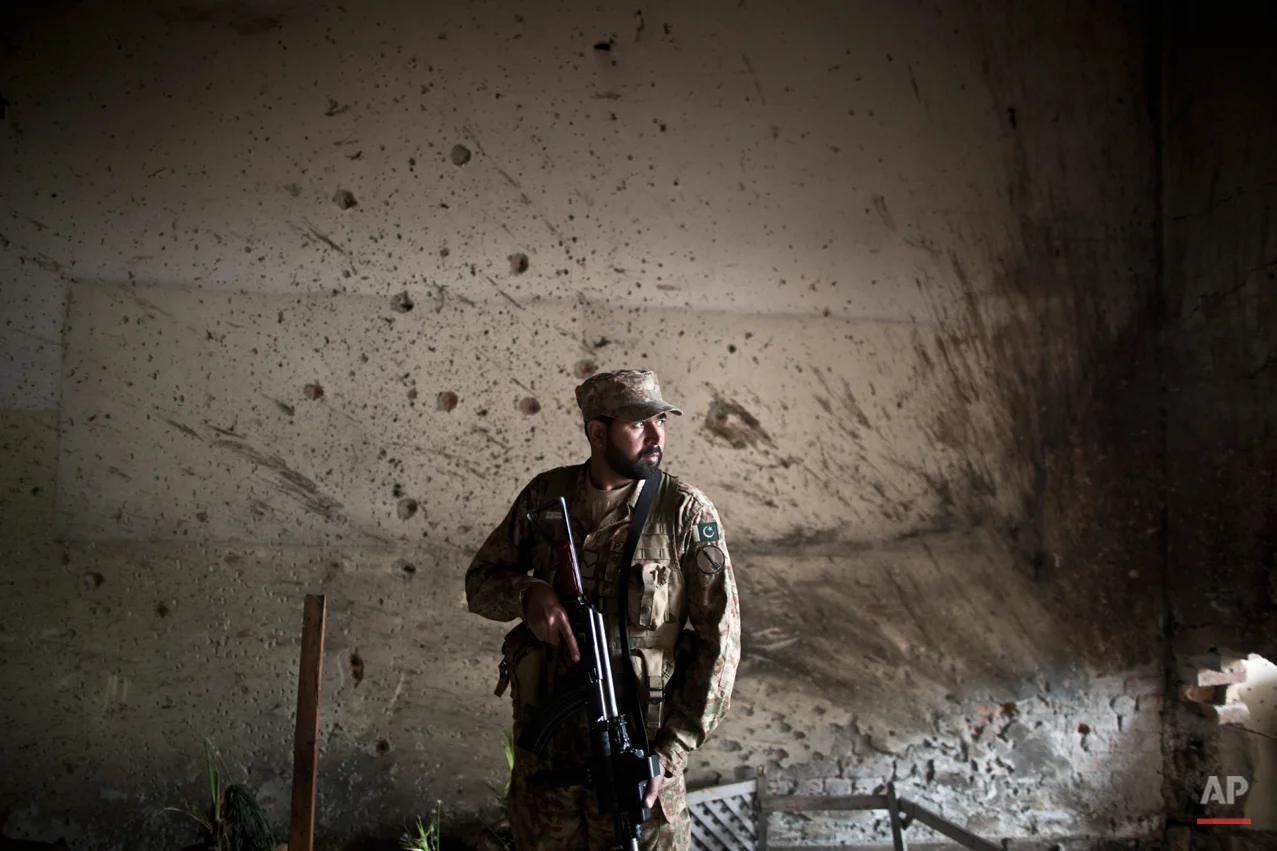 A Pakistani army officer, stands in front of a wall riddled with bullet marks, inside the Army Public School attacked last Tuesday by Taliban gunmen, in Peshawar, Pakistan, Thursday, Dec. 18, 2014. The Taliban massacre that killed more than 140 people, mostly children, at a military-run school in northwestern Pakistan left a scene of heart-wrenching devastation, pools of blood and young lives snuffed out as the nation mourned and mass funerals for the victims got underway. (AP Photo/Muhammed Muheisen)