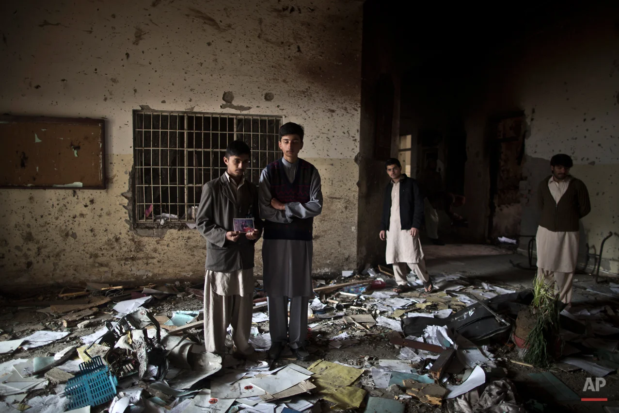 Pakistani students, Waqar Ahmad, left, and Uwais Naser, who survived last Tuesday's Taliban attack on a military-run school, stand at the site, one holding a picture of their headmaster Tahira Kazi, 58, who was killed in the attack, in Peshawar, Pakistan, Thursday, Dec. 18, 2014. The Taliban massacre that killed more than 140 people, mostly children, at a military-run school in northwestern Pakistan left a scene of heart-wrenching devastation, pools of blood and young lives snuffed out as the nation mourned and mass funerals for the victims got underway. (AP Photo/Muhammed Muheisen)