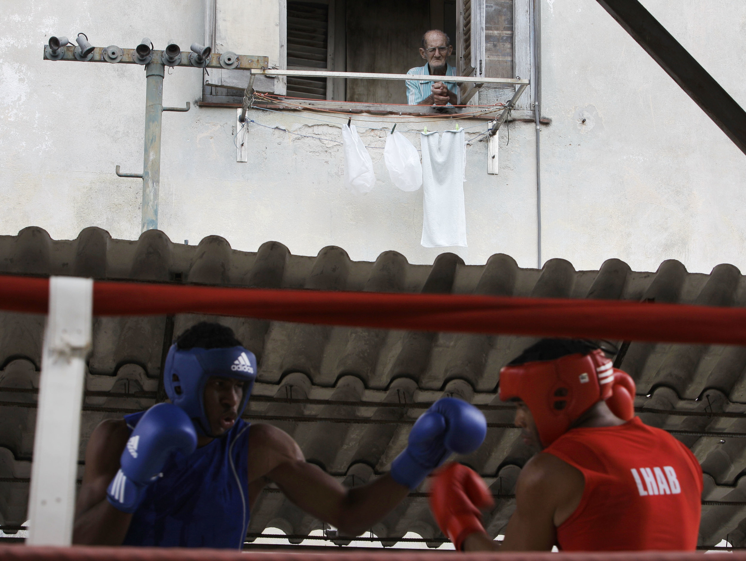  In this March 9, 2013 photo, a man peers from his home's window to watch boxer Frank Sanchez, left, fight with Julio Bernal during a boxing tournament at the Rafael Trejos boxing gym in Old Havana, Cuba. In 1961, two years after the Cuban Revolution