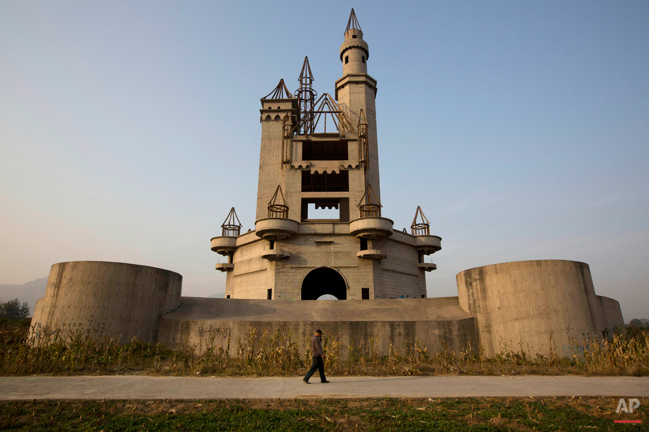  In this Oct. 18, 2014, photo, a man walks past the shell of a castle-like building that was once destined to be part of Asia's biggest amusement park in Beijing, China. Work halted on the project in 1998 due to financial problems and the site has be