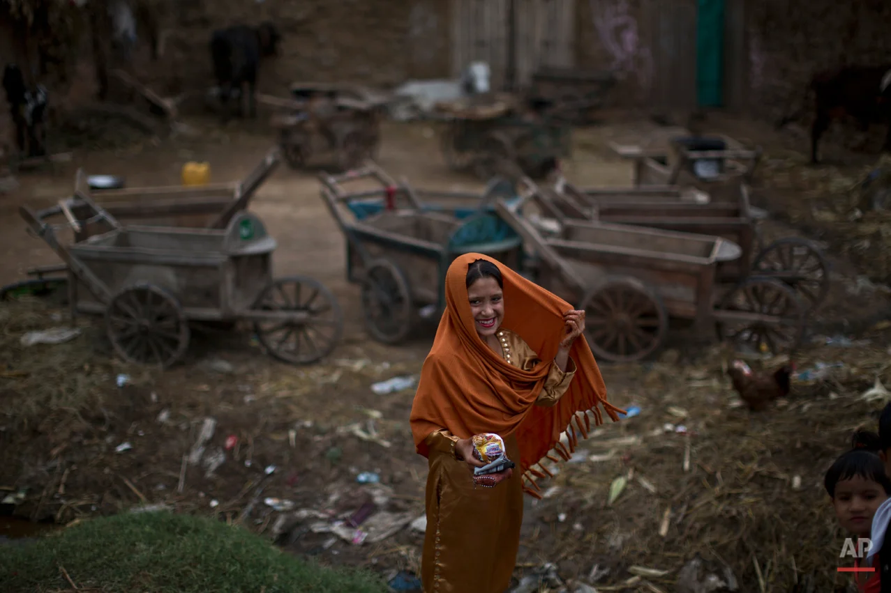 An Afghan refugee, wearing new clothes, smiles to her friends while she and others celebrate the Muslim holiday of Eid al-Adha, or Feast of Sacrifice, on the outskirts of Islamabad, Pakistan, Monday, Oct. 6, 2014. Muslims around the world celebrate Eid to commemorate what Muslims believe was Prophet Abraham's willingness to sacrifice his son Ismail. Because the holiday follows the Muslim lunar calendar that depends on sightings of the moon, the holiday starts on Monday in Pakistan. (AP Photo/Muhammed Muheisen)