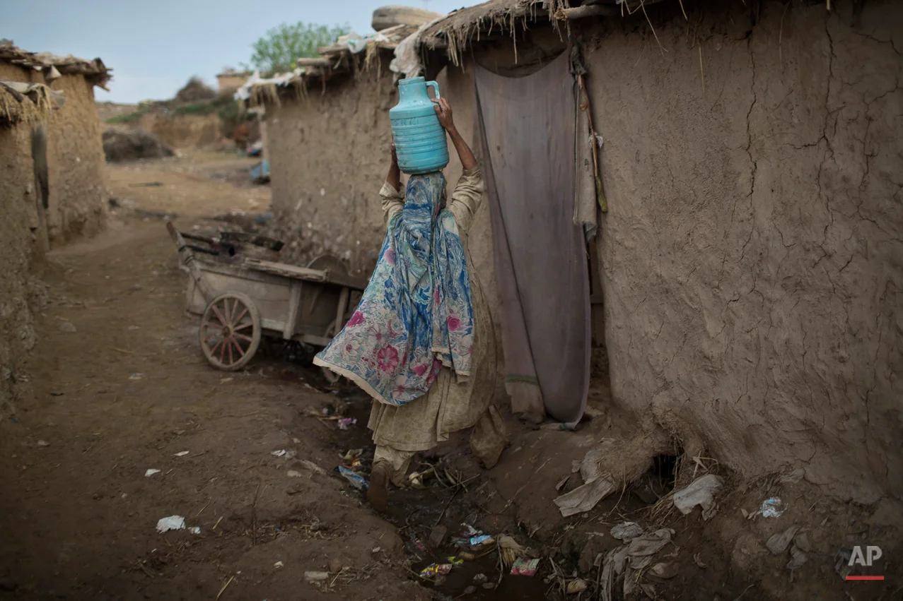 An Afghan refugee, enters her mud home carrying water on her head, during the Muslim holiday of Eid al-Adha, or Feast of Sacrifice, on the outskirts of Islamabad, Pakistan, Monday, Oct. 6, 2014. Muslims around the world celebrate Eid to commemorate what Muslims believe was Prophet Abraham's willingness to sacrifice his son Ismail. Because the holiday follows the Muslim lunar calendar that depends on sightings of the moon, the holiday starts on Monday in Pakistan. (AP Photo/Muhammed Muheisen)