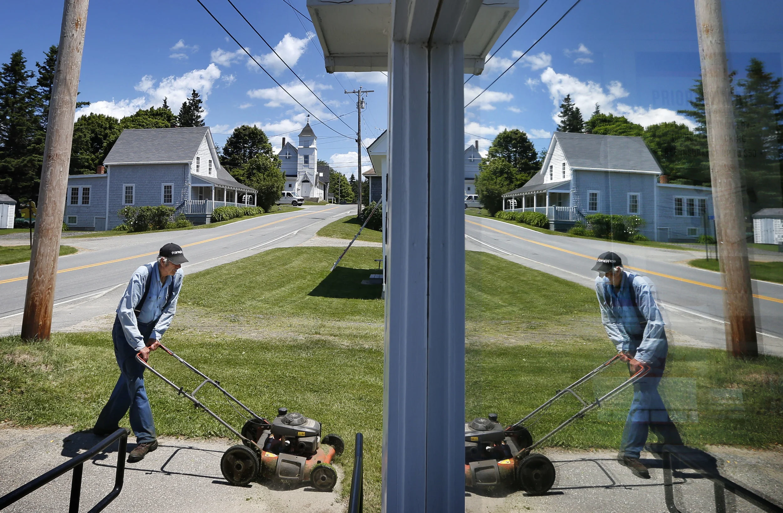 Ralph Russell, 76, is reflected in the front window of the post office, Thursday, June 19, 2014, in Port Clyde, Maine, where he has been cutting the lawn for almost 40 years. (AP Photo/Robert F. Bukaty)