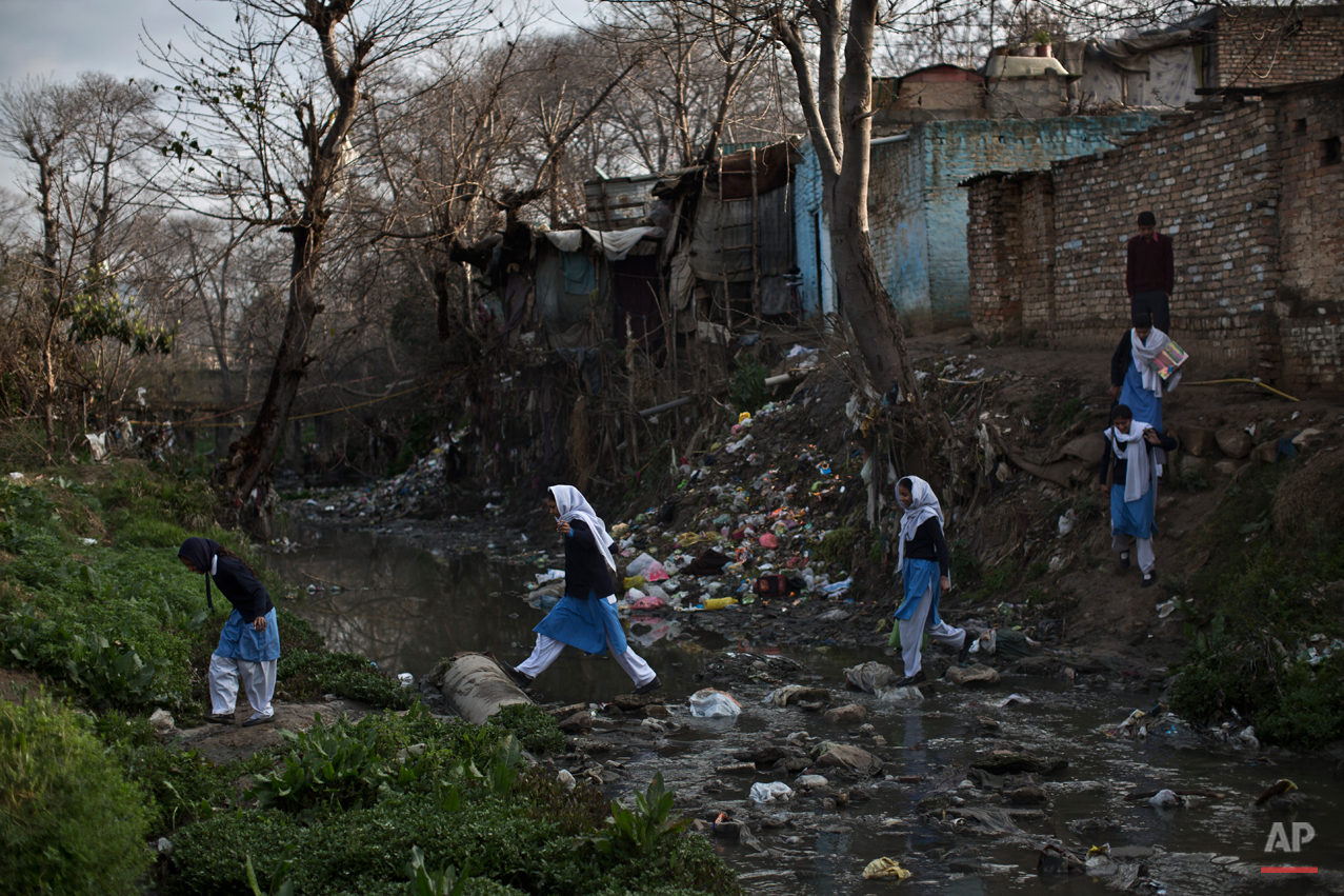  In this Tuesday, March 4, 2014, photo, Pakistani schoolgirls cross a stream of sewage and rubbish that separates their neighborhood from the main road, heading to their school in Islamabad, Pakistan. Malala Yousafzai's struggle for girls to be educa
