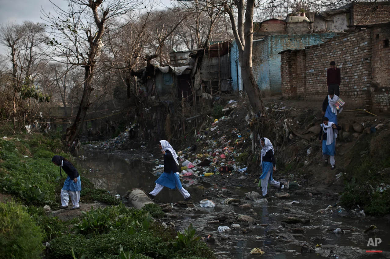 In this Tuesday, March 4, 2014, photo, Pakistani schoolgirls cross a stream of sewage and rubbish that separates their neighborhood from the main road, heading to their school in Islamabad, Pakistan. Malala Yousafzai's struggle for girls to be educated in a deeply conservative society led to her shooting by the Taliban two years ago, while her relentless campaign for women's was rewarded Friday, Oct. 10, 2014, by the recognition of her work as she was jointly awarded the Nobel Peace Prize. (AP Photo/Muhammed Muheisen)