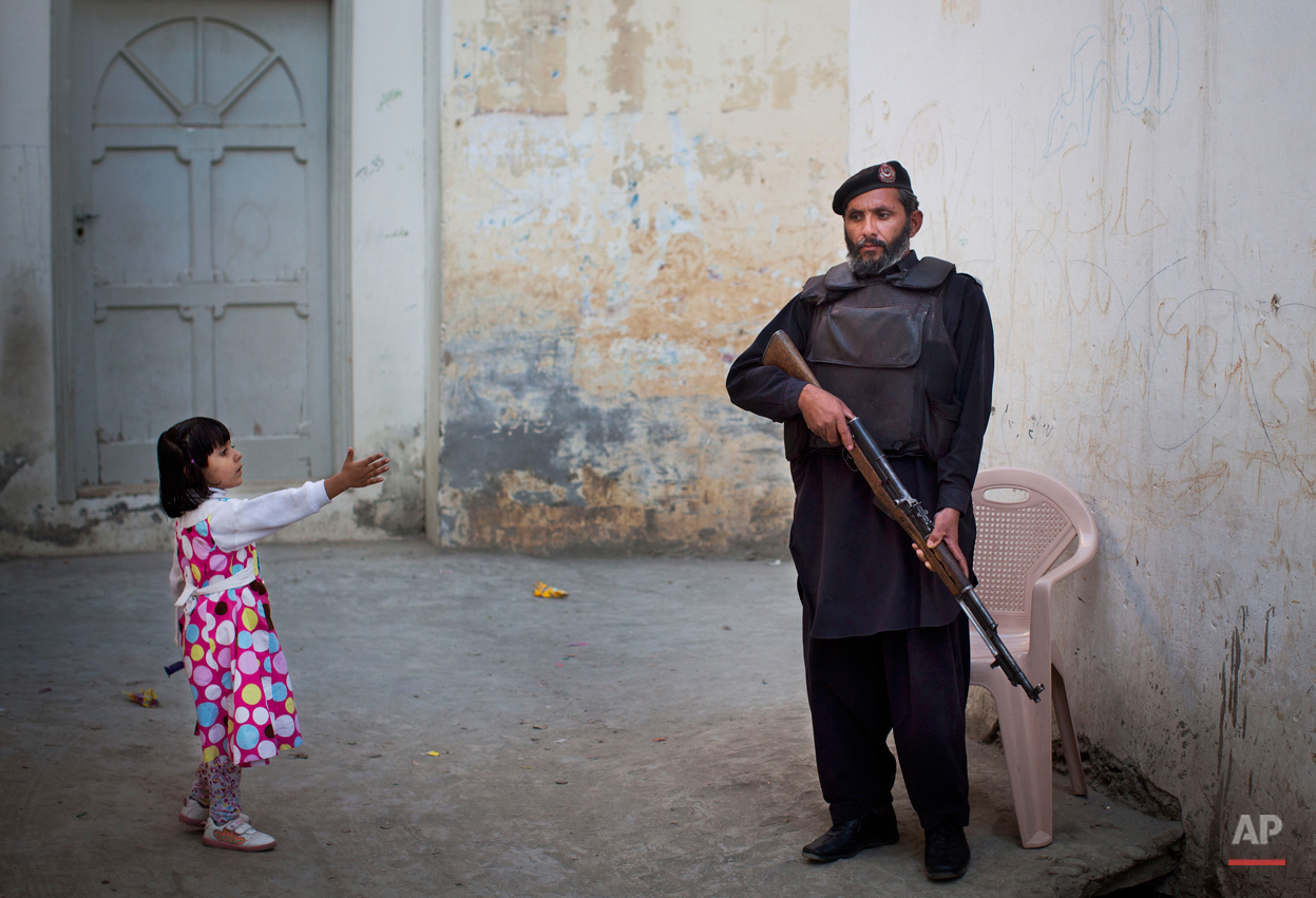  In this Wednesday, Nov. 15, 2012 photo, a young girl in her colorful dress reaches out to greet a Pakistani policeman securing the road outside Kainat Riaz's home in Mingora, Swat Valley, Pakistan. Malala Yousafzai's struggle for girls to be educate