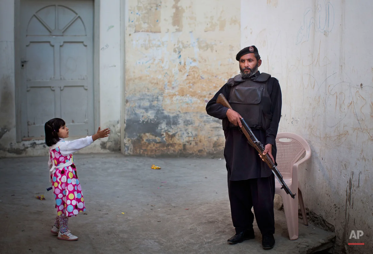 In this Wednesday, Nov. 15, 2012 photo, a young girl in her colorful dress reaches out to greet a Pakistani policeman securing the road outside Kainat Riaz's home in Mingora, Swat Valley, Pakistan. Malala Yousafzai's struggle for girls to be educated in a deeply conservative society led to her shooting by the Taliban two years ago, while her relentless campaign for women's rights was rewarded Friday, Oct. 10, 2014, by the recognition of her work as she was jointly awarded the Nobel Peace Prize. ( AP Photo/Anja Niedringhaus)