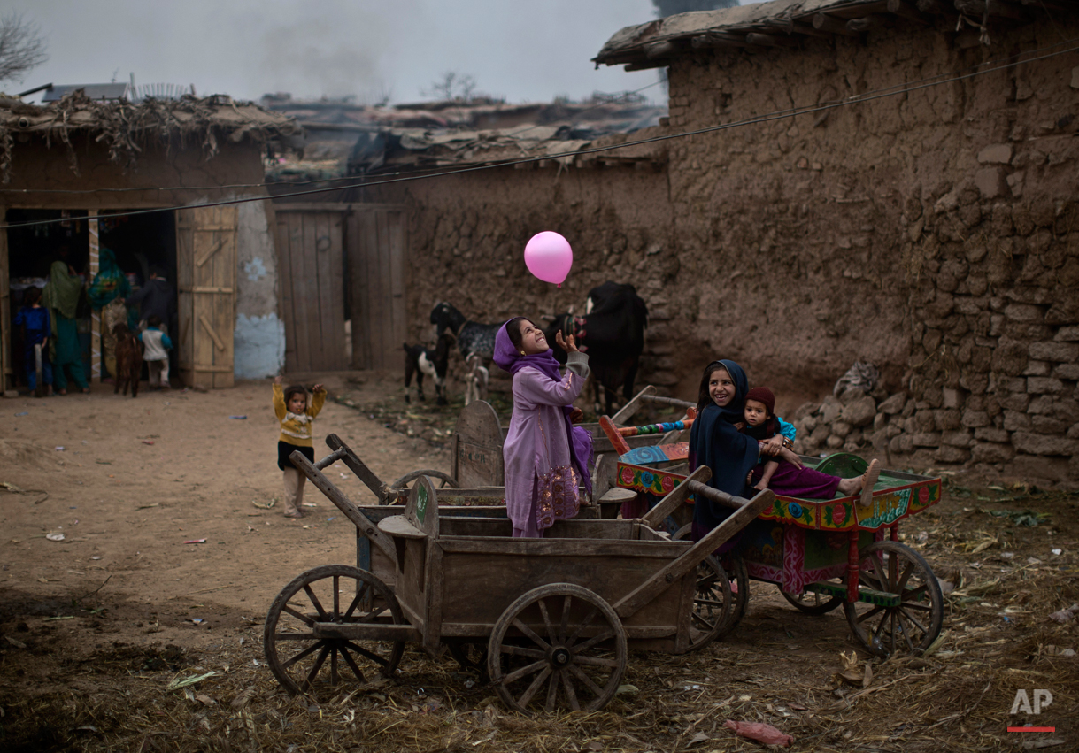 An Afghan refugee girl, right, holding her younger brother, sits on a wooden-cart looking at her friend playing with a balloon, in a poor neighborhood on the outskirts of Islamabad, Pakistan, Sunday, Feb. 2, 2014. (AP Photo/Muhammed Muheisen) 