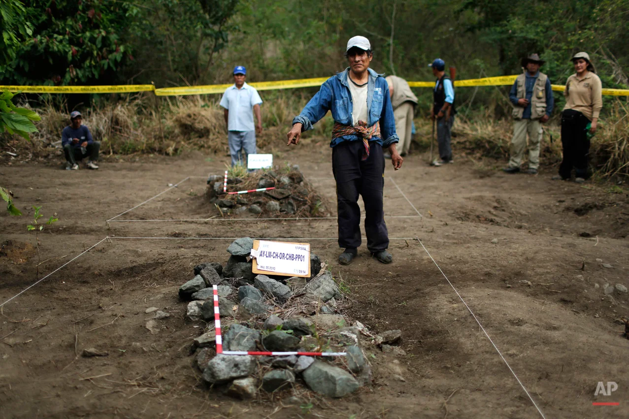 In this Sept. 4, 2014 photo, Felix Casa, right center, and Cipriano Huaman, back left, pose for the visual anthropologist, pointing to the graves where they believe their relatives were buried during an exhumation of mass graves of villagers slain by security forces, in the Paccha village of Chungui, Peru. In all, 21 sets of human remains were recovered, including those of eight children and a fetus, said Luis Rueda, the forensic archaeologist overseeing the dig. (AP Photo/Rodrigo Abd)