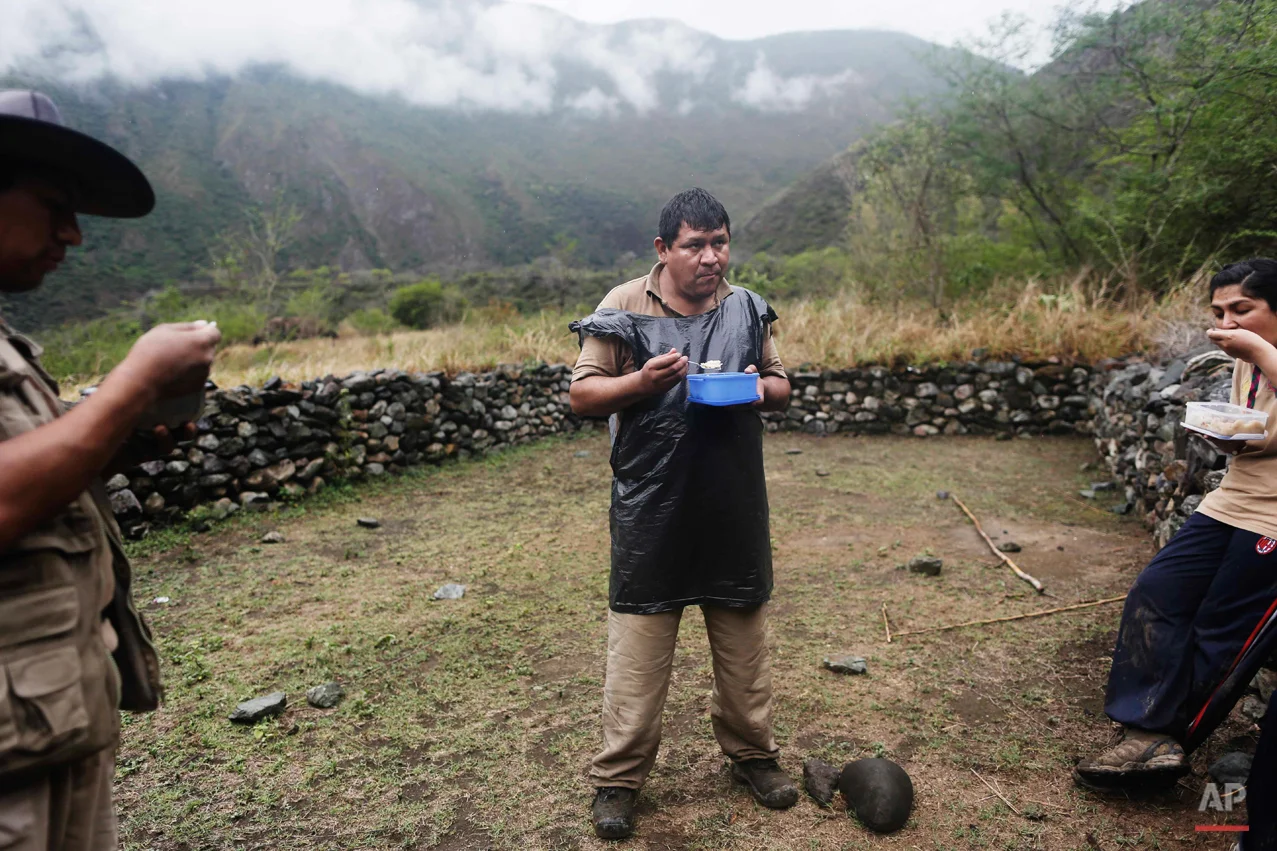In this Sept. 5, 2014 photo, forensic anthropologists; Rolando Alvarado, center; Soledad Mostacero, right; and Osvaldo Calcina, break to eat during an exhumation of a mass grave of villagers slain by government security forces, in the Paccha village of the Peru. Since 2003, the remains of slightly more than 2,400 victims of the 1980-2000 internal conflict have been recovered, but the bodies of an estimated 12,000 more, mostly poor, Quechua-speaking farmers, are believed to remain unearthed. (AP Photo/Rodrigo Abd)