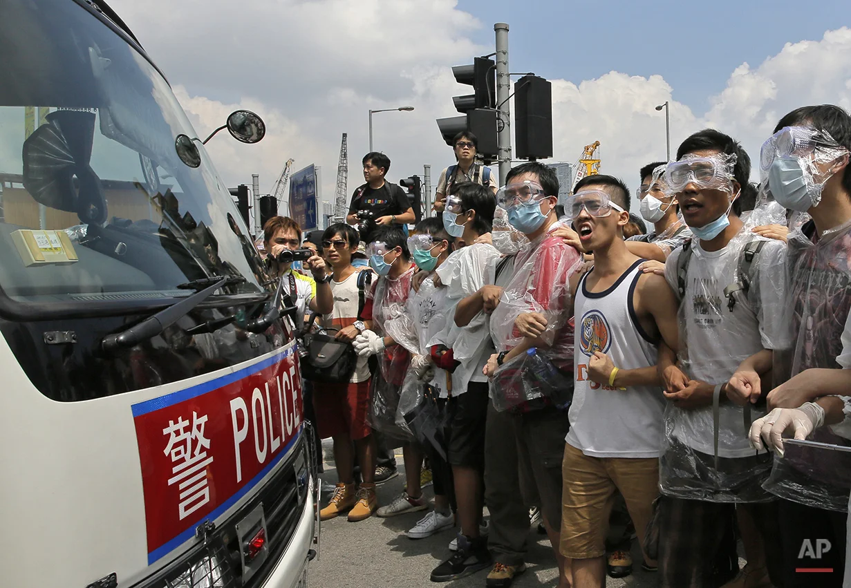 Protesters wear masks and goggles to protect themselves from pepper spray while blocking a police car outside the government headquarters in Hong Kong, Sunday, Sept. 28, 2014. Hong Kong activists kicked off a long-threatened mass civil disobedience protest Sunday to challenge Beijing over restrictions on voting reforms, escalating the battle for democracy in the former British colony after police arrested dozens of student demonstrators. (AP Photo/Vincent Yu)