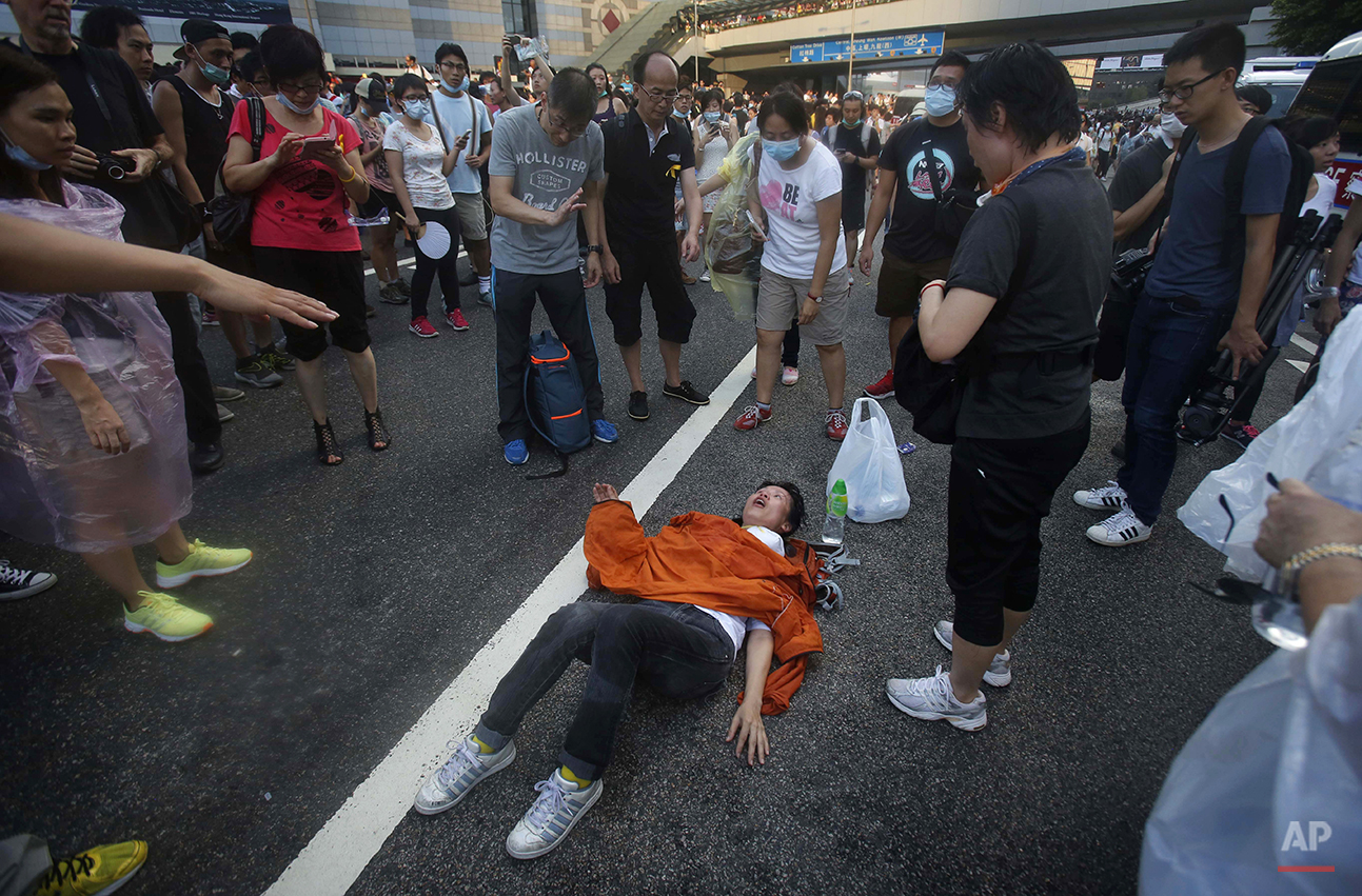  A woman collapses on a street as riot police fire tear gas and pepper spray into the crowds of thousands of protesters surrounding the government headquarters in Hong Kong Sunday, Sept. 28, 2014. Hong Kong police used tear gas on Sunday and warned o