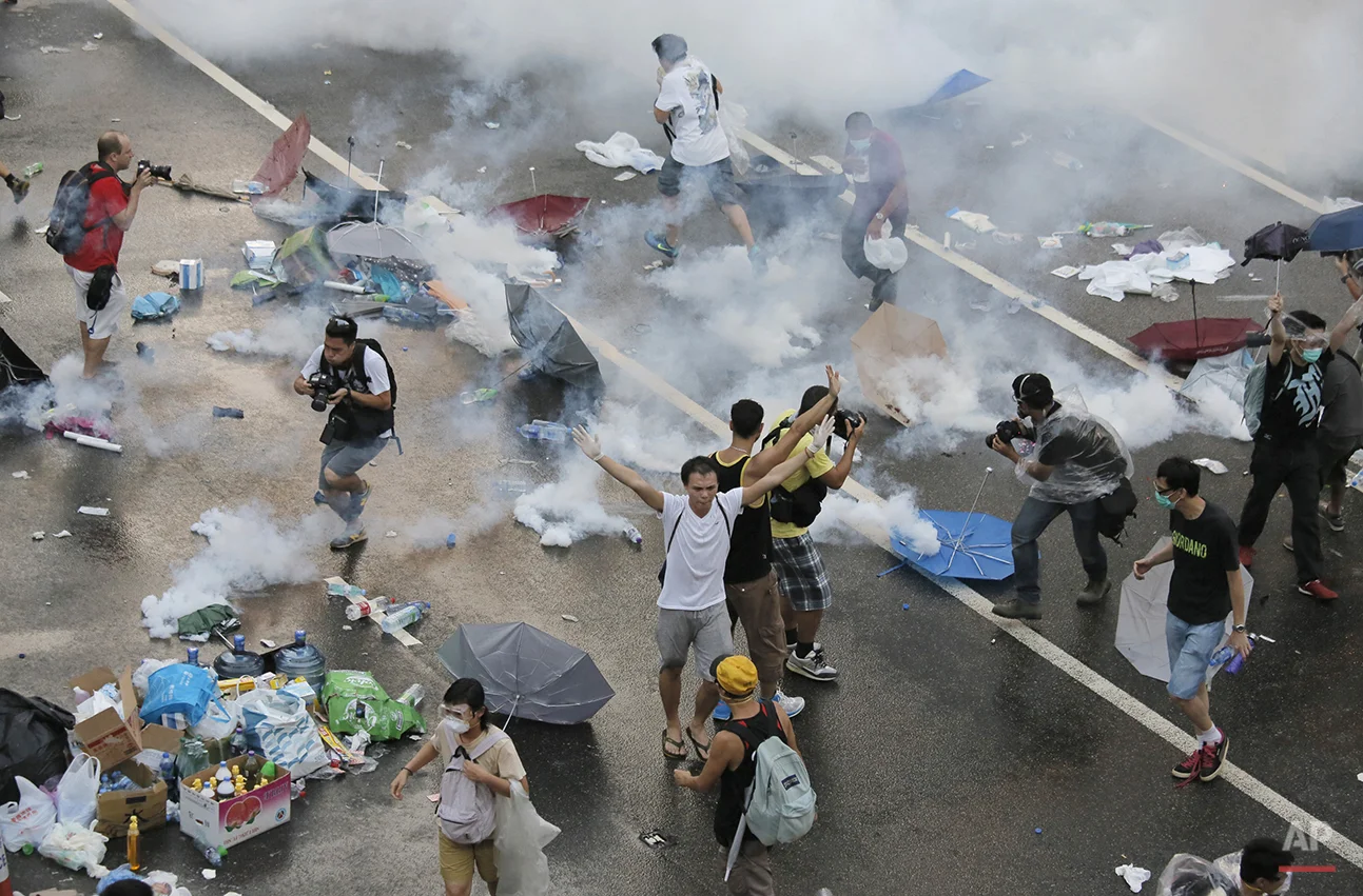 Protesters walk through tear gas used by riot police against protesters after thousands of people blocked a main road at the financial central district in Hong Kong, Sunday, Sept. 28, 2014. Authorities launched their crackdown after the protest spiraled into an extraordinary scene of chaos as the crowd jammed a busy road and clashed with officers wielding pepper spray. (AP Photo/Vincent Yu)
