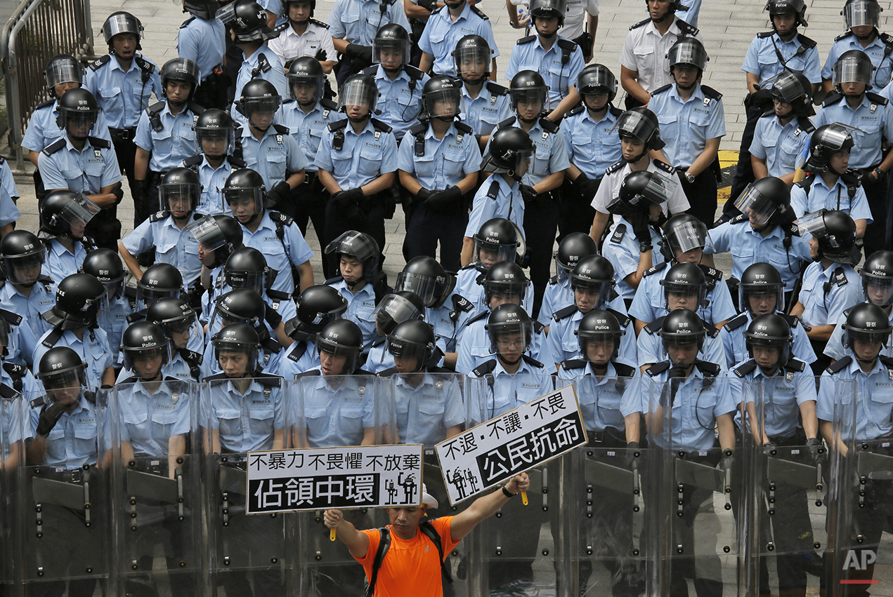  A protester raises placards that read "Occupy Central," left, and "Civil disobedience" in front of riot policemen outside the government headquarter in Hong Kong Saturday, Sept. 27, 2014. Riot police on Saturday arrested scores of students who storm