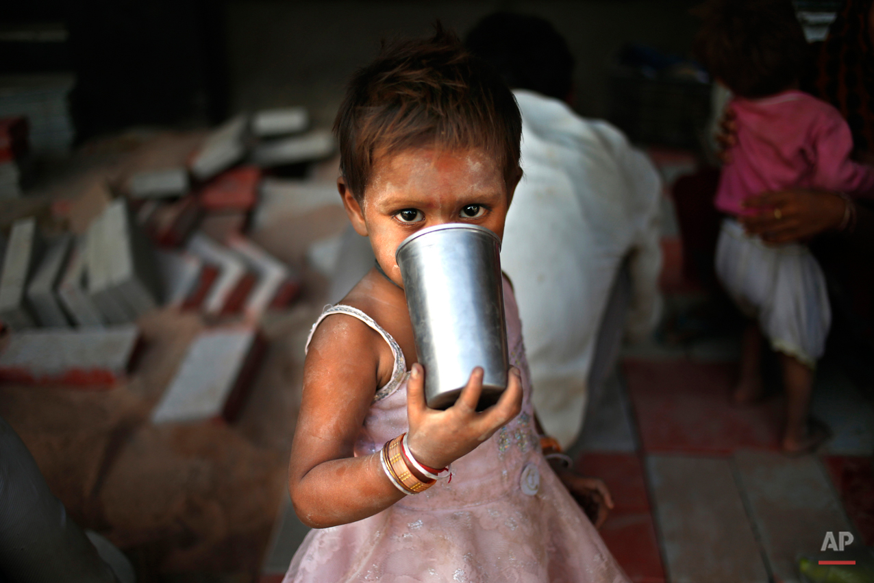  A small girl drinks water from a steel glass as her parents construct a pavement in New Delhi, India, Wednesday, May 8, 2013. The capital is reeling under a heat wave with temperatures touching 40.8 degrees Celsius (105 degrees Fahrenheit) Tuesday, 