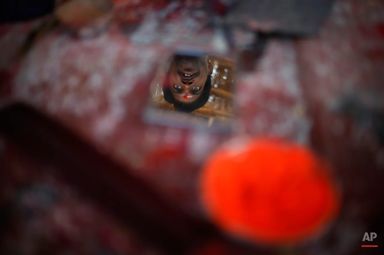 A comb and a bowl of vermillion powder lie on a shelf as a Hindu holy man is reflected in a mirror kept for the use of devotees after bathing, near Sangam, confluence of Hindu holy rivers of Ganges, Yamuna and the mythical Saraswati, at the Maha Kumbh festival in Allahabad, India, Thursday, Feb. 14, 2013. Millions of Hindu pilgrims are attending the Maha Kumbh festival, which is one of the world's largest religious gatherings that lasts 55 days and falls every 12 years. During the festival pilgrims bathe in the holy Ganges River in a ritual they believe can wash away their sins. (AP Photo/ Saurabh Das)
