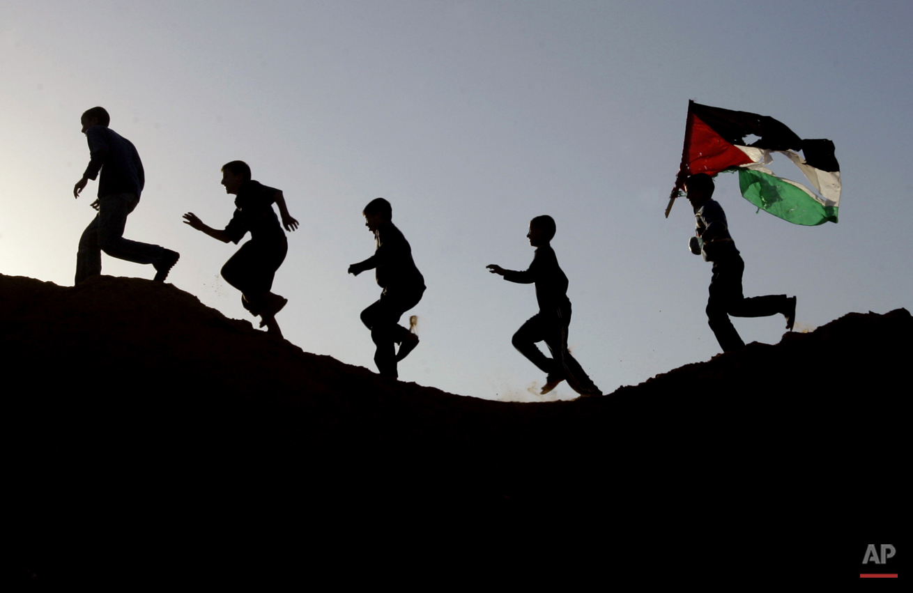  Palestinian youths, one carrying a Palestinian flag, run on a hillside after Israeli troops pulled out of Beit Lahiya, in the northern Gaza Strip, Sunday, Nov. 26, 2006. A truce meant to end five months of deadly Israeli-Palestinian clashes took hol