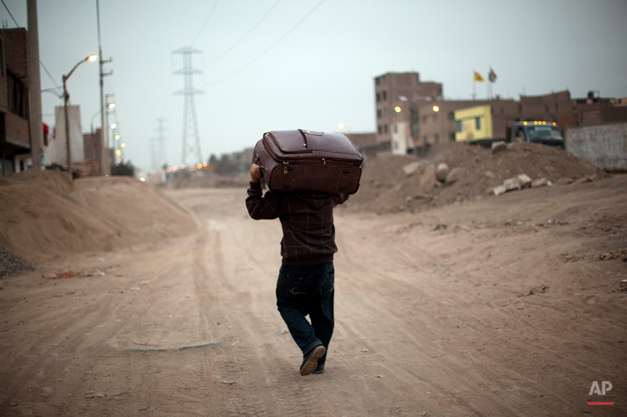  A man hauls a suitcase on along a dirt road in the Santa Rosa Chuquitanta neighborhood in Lima, Peru, Thursday, July 25, 2013. (AP Photo/Rodrigo Abd) 