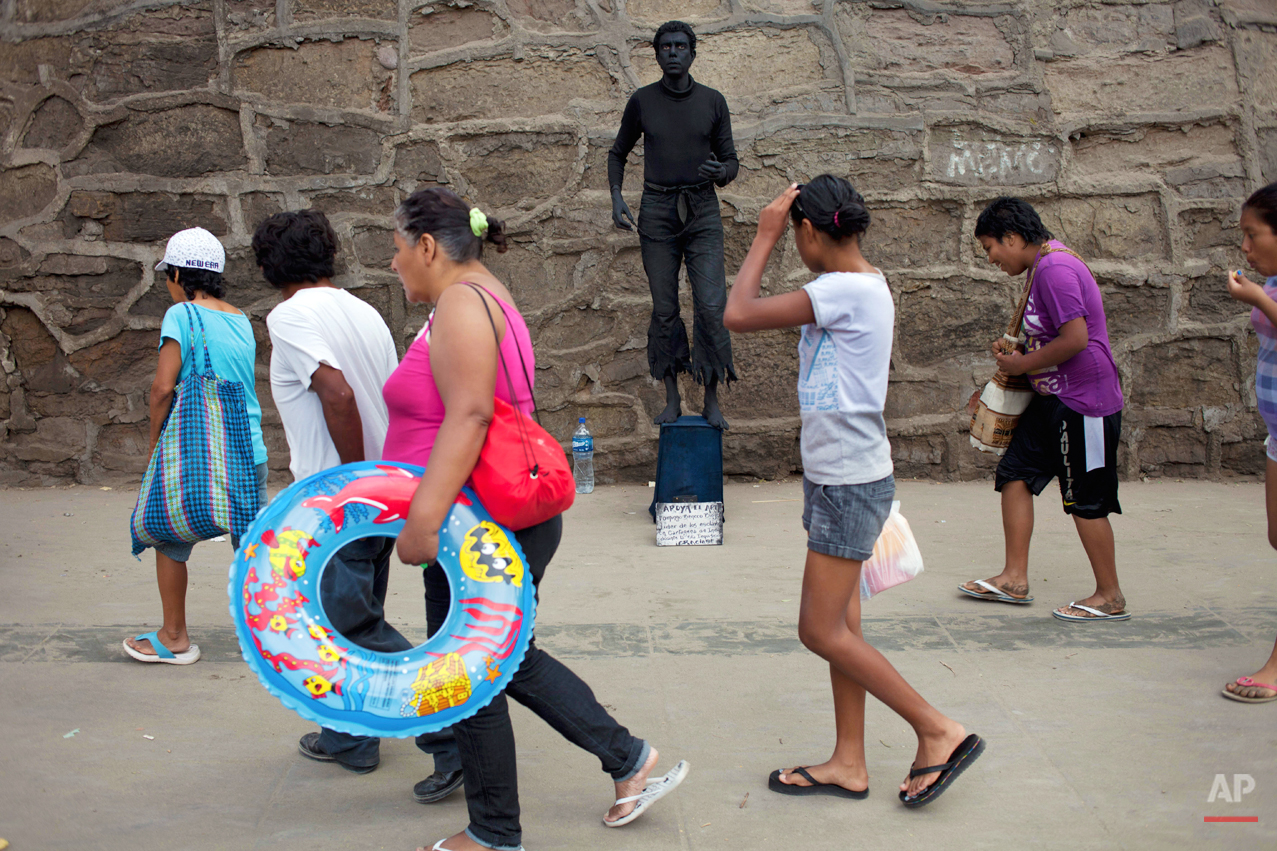 People walk past Martin Flores, top, from Colombia, as he performs as a living statue in Lima, Peru, Tuesday, Jan. 22, 2013. (AP Photo/Rodrigo Abd)