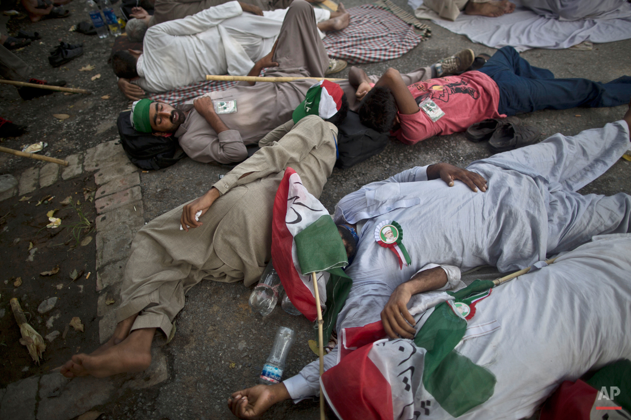 Supporters of fiery anti-government cleric Tahir-ul-Qadri, wearing pins showing his image, sleep on the ground, after marching all night long from Lahore to Islamabad, at the site of a rally in Islamabad, Pakistan, Saturday, Aug. 16, 2014. Qadri led massive rallies Saturday in Pakistanís capital, demanding Prime Minister Nawaz Sharif step down over alleged fraud in last yearís election in front of thousands of protesters. (AP Photo/Muhammed Muheisen)