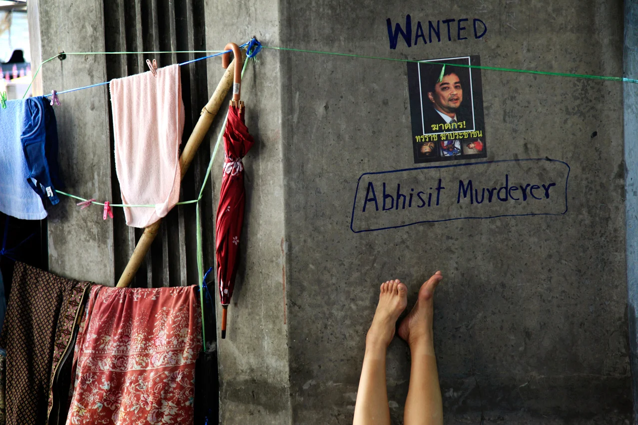 A woman sleeps under a defaced poster with a picture of Thailand's Prime Minister Abhisit Vejjajiva in the anti-government encampment on Monday May 10, 2010 in Bangkok, Thailand. Thailand's prime minister pleaded Sunday for an end to two months of street protests paralyzing part of the capital and an acceptance of his reconciliation plan that has been stalled by fresh violence. (AP Photo/Wong Maye-E)