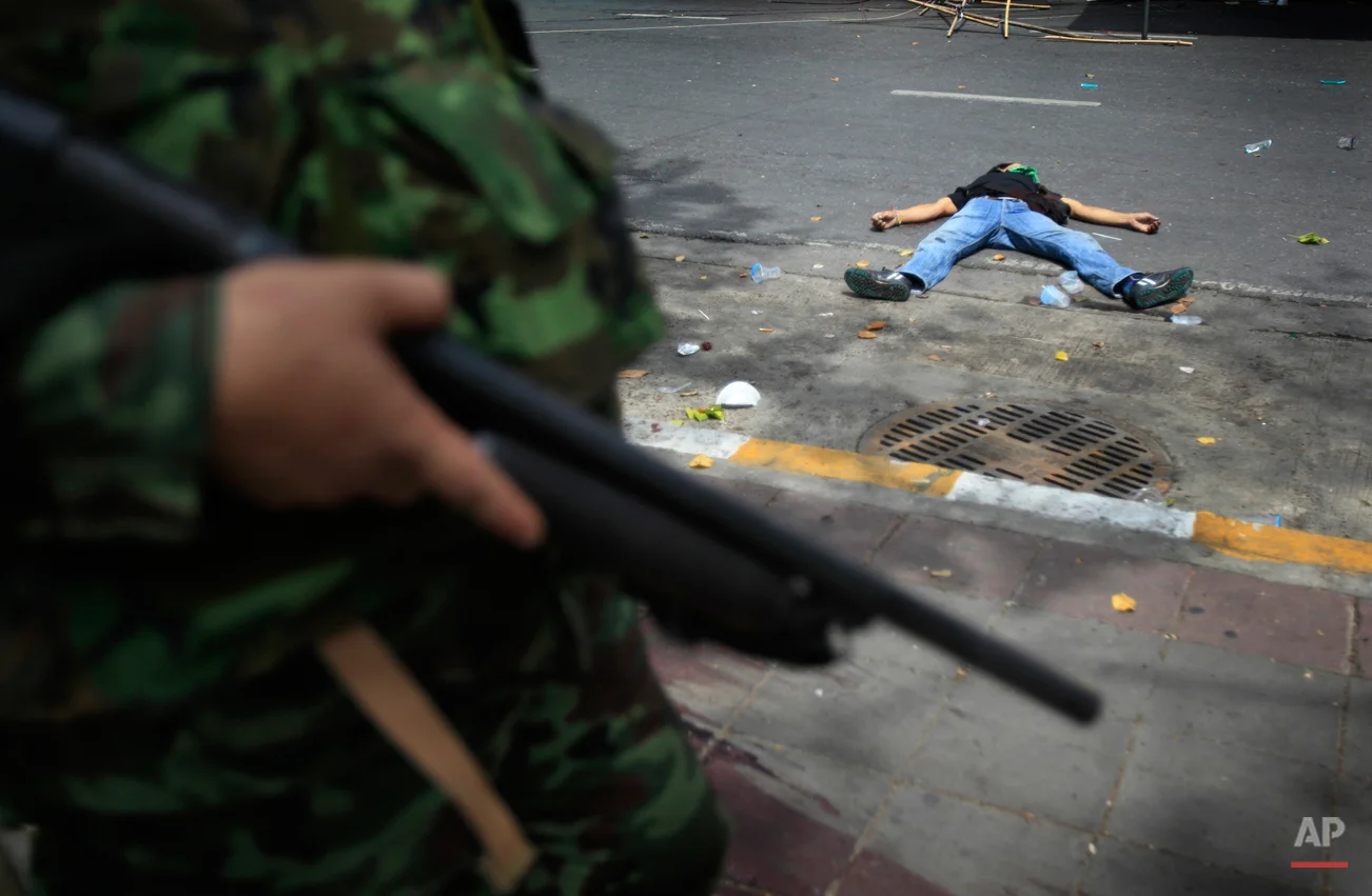 Thai soldiers storm into anti-government protesters' encampment while a protester lies dead on Wednesday May 19, 2010, in Bangkok, Thailand. Downtown Bangkok became a raging battleground Wednesday as the army stormed a barricaded protest camp and the Red Shirt leadership surrendered, enraging demonstrators who fired grenades and set fires that cloaked the skyline in a black haze. (AP Photo/Wong Maye-E )
