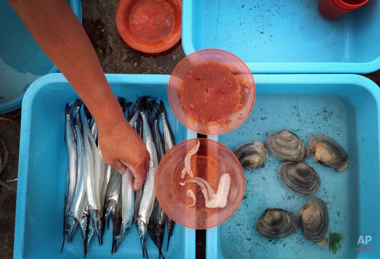 A store vendor picks fish for her customers to cook over a pot of burning charcoal along the pier leading to Jangdok Island, Monday, July 28, 2014, in Wonsan, North Korea. North Korea has been creating special zones across the country to try to boost tourism and Wonsan, long a favorite of North Korean vacationers, is being pushed as a prime destination for international travelers. (AP Photo/Wong Maye-E)