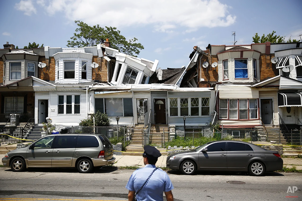 A police officer stands by two collapsed row houses Monday, July 7, 2014, in Philadelphia. Authorities say no injuries were reported in the collapses. (AP Photo/Matt Rourke)