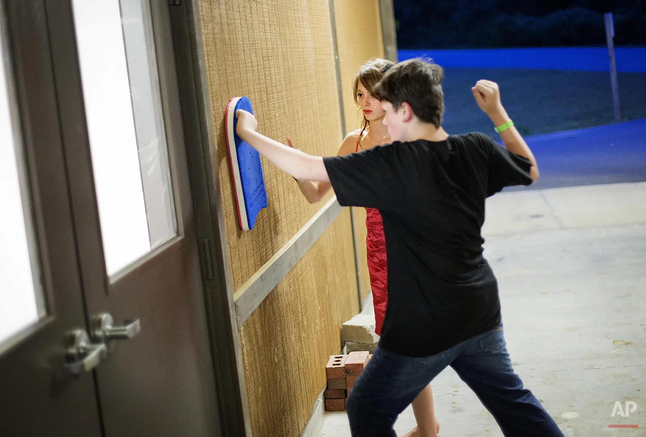 In this Thursday, July 17, 2014 photo, Kristin Moorehead, 13, of Tampa, Fla., left, comforts A.J. Dorough, 13, of Covington, Ga., as he uses a foam kick board to avoid hurting himself during a tic where he feels the urge to hit his hand against a wall at Camp Twitch and Shout, a camp for children with Tourette's Syndrome in Winder, Ga. The two met at the camp four years ago and always attend the dance together on the camp's final night. "We help each other out," says Moorehead, who first tried deep breathing exercises with Dorough to get through the tic. After it didn't work she could only comfort him while he hit the wall to get the tic out. "The hard part is where you have to stand by and watch, you feel so helpless." (AP Photo/David Goldman)