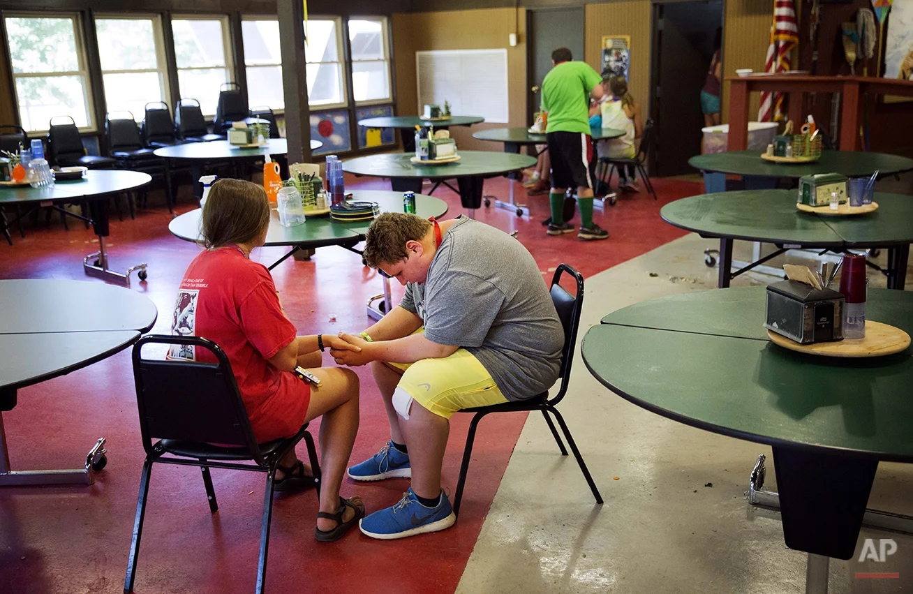 In this Thursday, July 17, 2014 photo, camper Andrew Nail, 14, of Atlanta, right, sits with counselor Danielle Kaidon, 21, as she helps him get through a tic where he feels the urge to hold someone's hand following lunch hour at Camp Twitch and Shout, a camp for children with Tourette's Syndrome in Winder, Ga. The two sat there for about ten minutes until Nail felt the urge pass. (AP Photo/David Goldman)