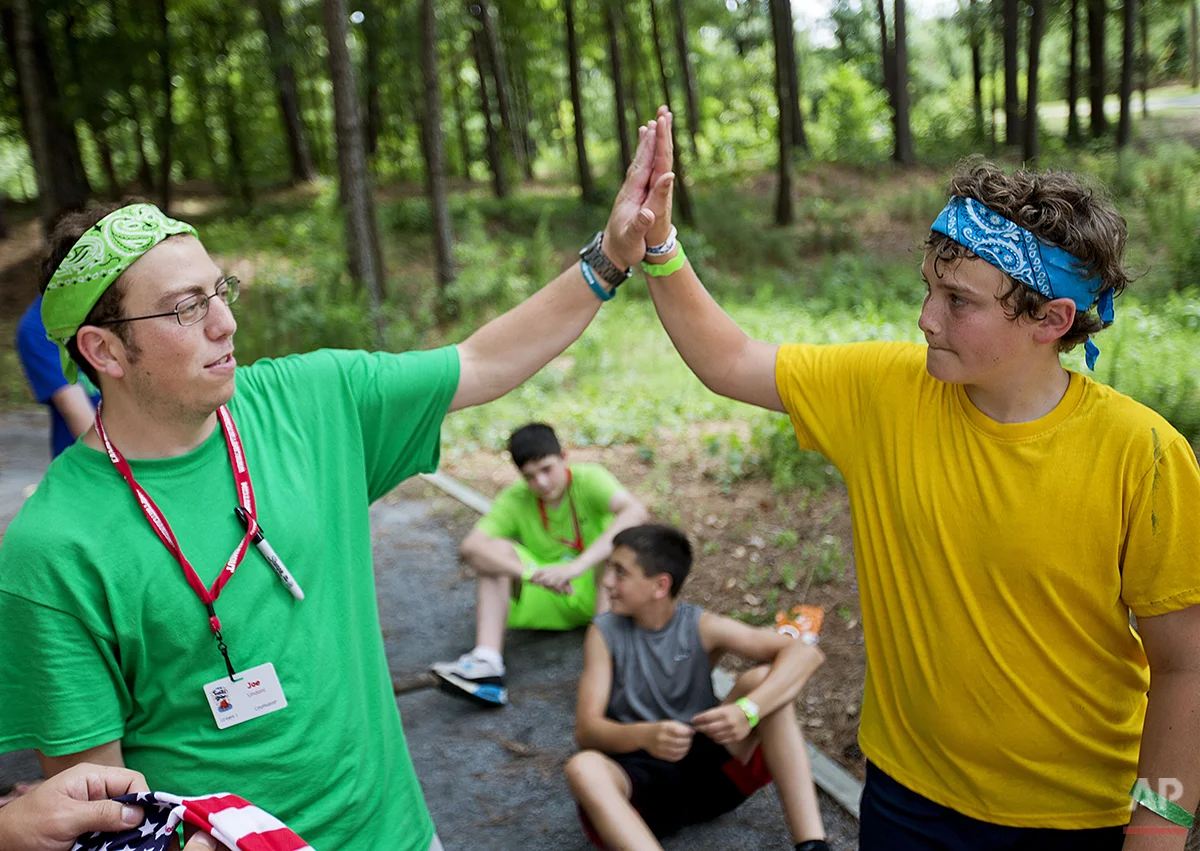 In this July 15, 2014 photo, Logan Henderson, 13, of Blairsville, Ga., right, is high-fived by counselor Joe Sindoni, 25, after completing a rope course in the trees at Camp Twitch and Shout, a camp for children with Tourette Syndrome in Winder, Ga. (AP Photo/David Goldman)