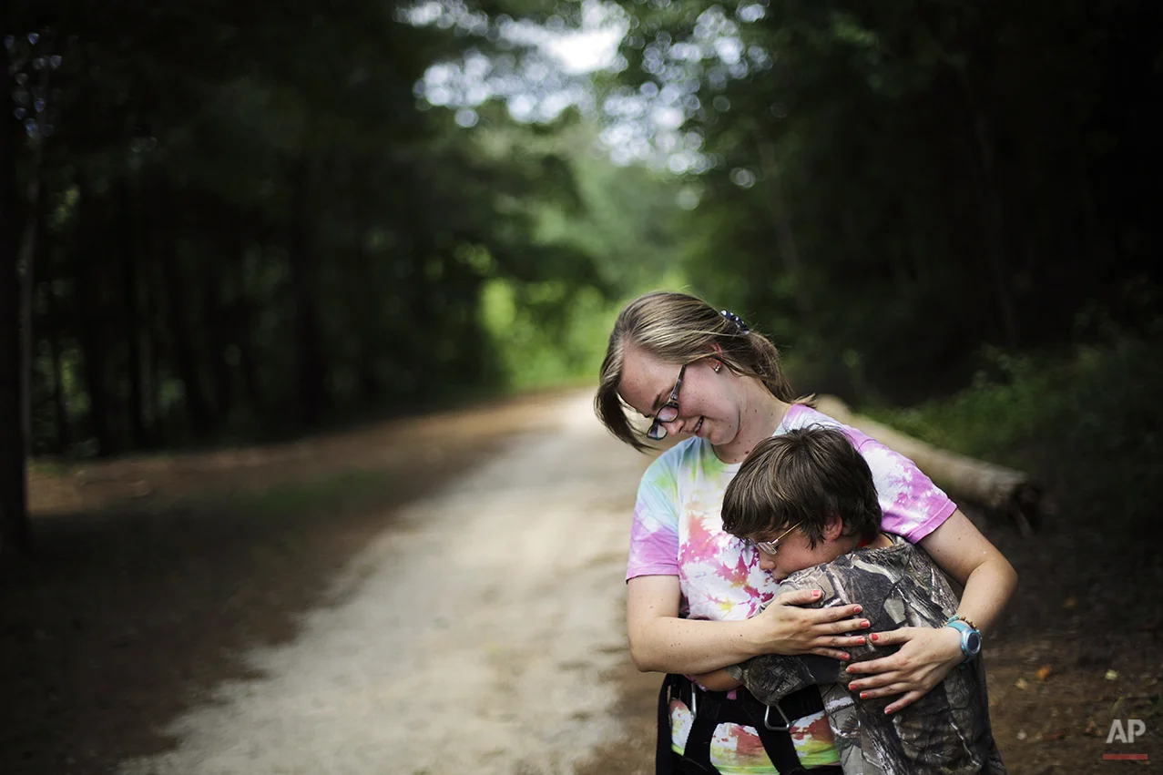 In this July 15, 2014 photo, Liam Harrison, 13, of Nashville, Tenn., right, embraces camp worker Katie Lesesne, 21, while experiencing a tic where he feels the urge to hug someone in proximity at Camp Twitch and Shout, a camp for children with Tourette Syndrome in Winder, Ga. "When I get the feeling, I just want to squeeze someone," explains Harrison. "When I let go it makes me happy. It feels so awesome like I'm gaining something. It makes me feel a lot better." (AP Photo/David Goldman)