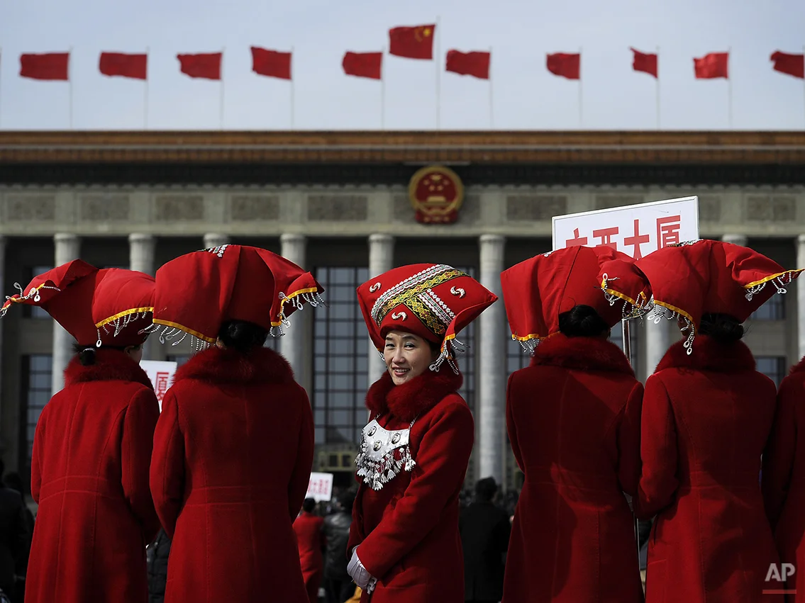 A Chinese usher in ethnic headwear, center, look back as they pose for photograph on the Tiananmen Square during the opening session of the National People's Congress at the Great Hall of the People in Beijing, Friday, March 5, 2010. (AP Photo/Andy Wong)