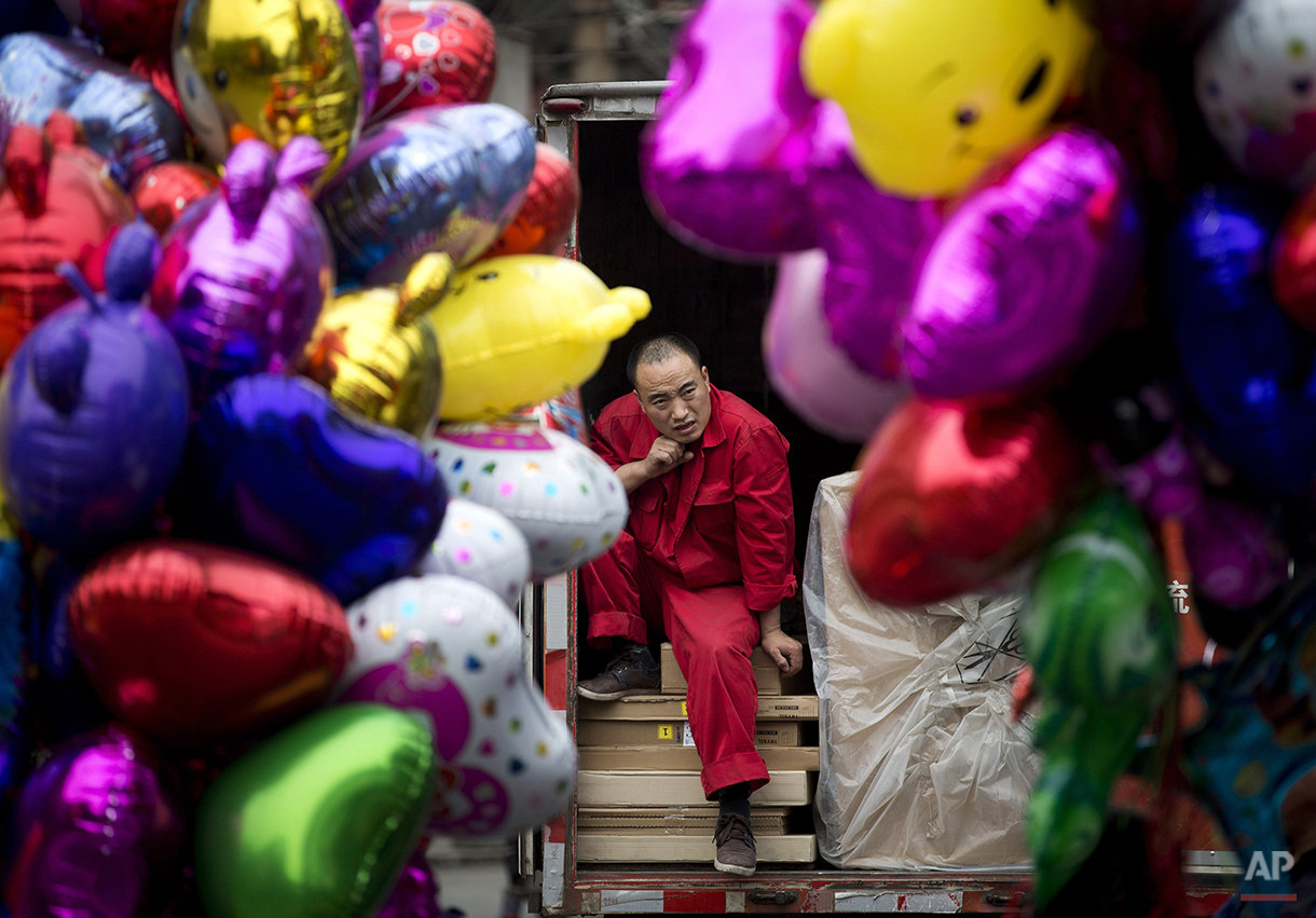  A worker takes a break on a truck loaded with goods in between balloons sold by vendors in Beijing, China Thursday, April 10, 2014. China reported an unexpected contraction in exports in March, raising the danger of job losses as Beijing tries to ov