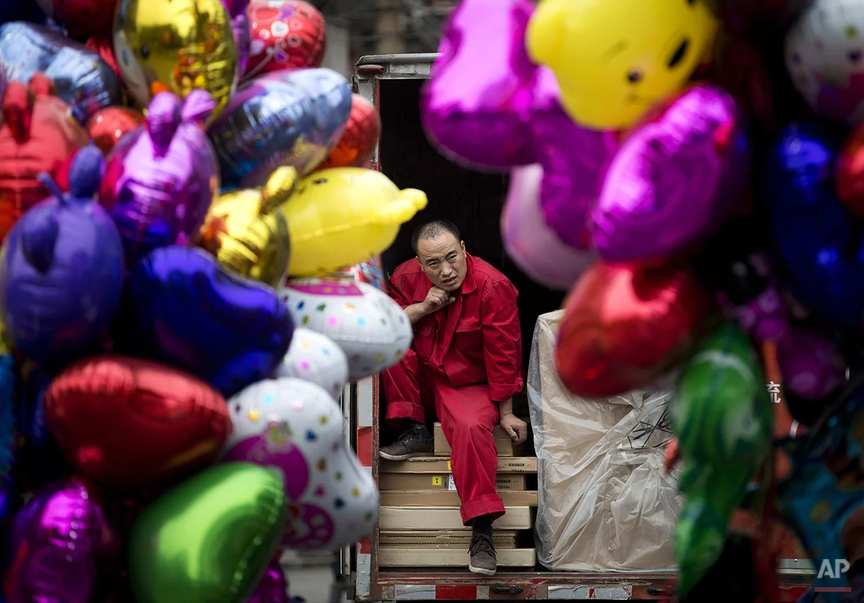 A worker takes a break on a truck loaded with goods in between balloons sold by vendors in Beijing, China Thursday, April 10, 2014. China reported an unexpected contraction in exports in March, raising the danger of job losses as Beijing tries to overhaul its slowing economy. (AP Photo/Andy Wong)
