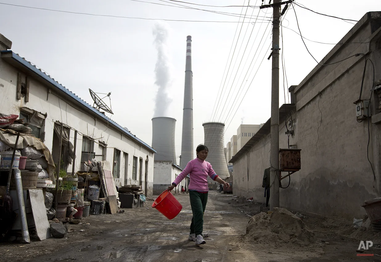 A woman walks through a neighborhood near a coal-fired power plant in Beijing on Friday, April 12, 2013. China, the world's largest producer of carbon dioxide, is directly feeling the man-made heat of global warming, scientists conclude in the first study to link the burning of fossil fuels to one country's rise in its daily temperature spikes. (AP Photo/Andy Wong)