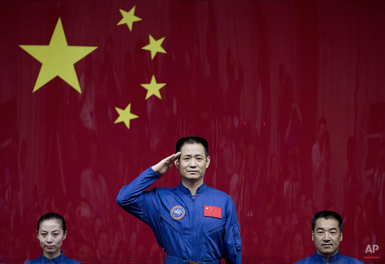  Chinese astronaut Nie Haisheng, center, salutes from behind a glass enclosure next to Wang Yaping, left, and Zhang Xiaoguang, right, as they meet the press at the Jiuquan satellite launch center near Jiuquan in western China's Gansu province, Monday