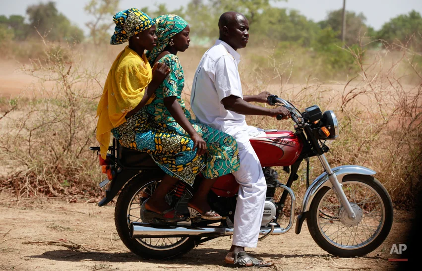 In this photo taken Sunday, May 18, 2014, Joy Bishara, left, and Hadiza Fali, centre, two of the school girls that escaped being kidnapped by Islamist extremists by jumping off a truck, are photographed on a motor taxi outside her school, in Chibok, Nigeria. More than 200 schoolgirls were kidnapped from a school in Chibok in Nigeria's north-eastern state of Borno on April 14. Boko Haram claimed responsibility for the act. (AP Photo/Sunday Alamba)