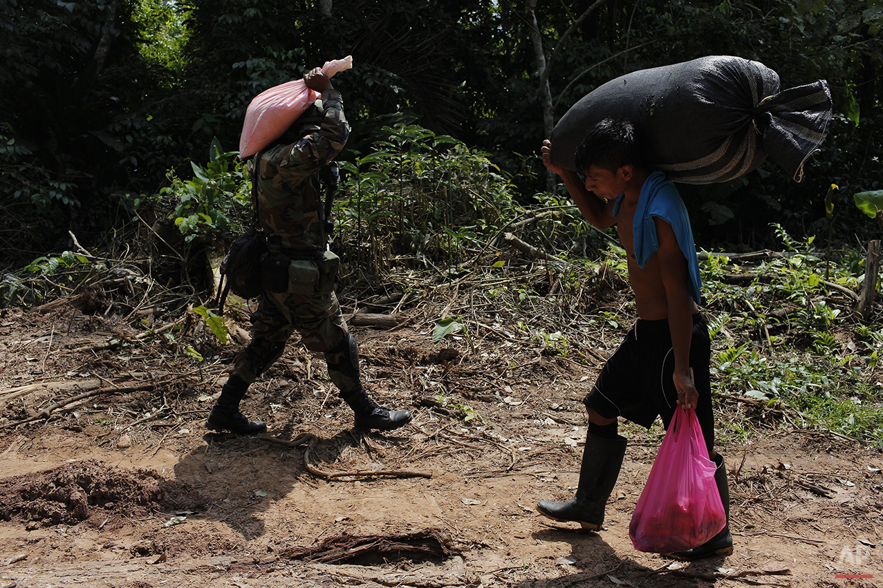  In this July 31, 2015 photo, a counternarcotics special forces officer carries a bag of ammonium nitrate explosives that will be used to crater a clandestine airstrip, as a local villager carries a sack filled with coca leaves near Ciudad Constituci
