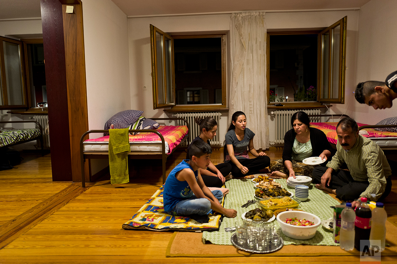 In this Tuesday, Sept. 13, 2016 photo, Yazidi migrant family, from Sinjar, Iraq, from right to left, Dilshad Qasu, 18, Samir Qasu, 46, Bessi Qasim, 43, Delphine Qasu, 19, Dunia Qasu, 14, and Dildar Qasu, 11, sit on the ground while having their dinner at their apartment in Elzach, Germany.(AP Photo/Muhammed Muheisen)