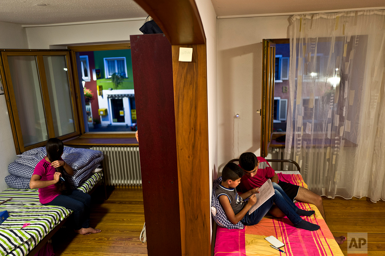  In this Wednesday, Sept. 14, 2016 photo, Dunia Qasu, 14, left, sits on her bed combing her hair while her elder brother Dilshad, 18, helps his younger brother Dildar, 11, in his homework, at their apartment in Elzach, Germany. (AP Photo/Muhammed Muh