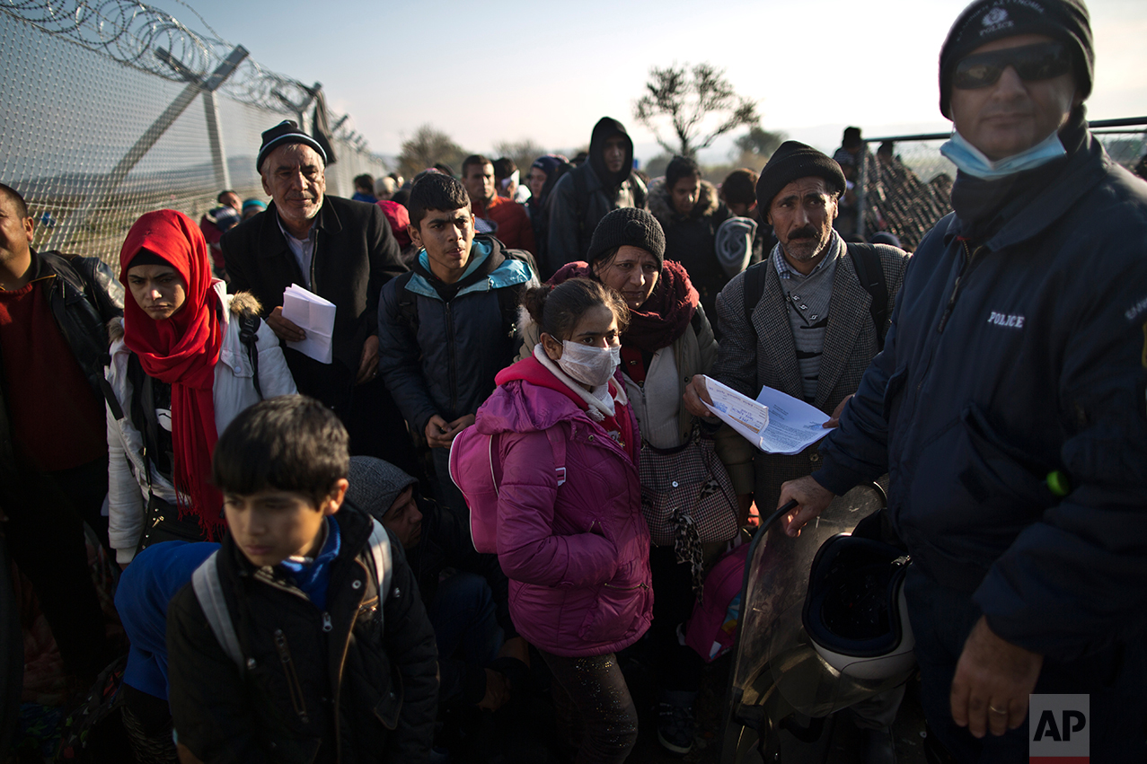  In this Saturday, Dec. 5, 2015 photo, Yazidi refugee Samir Qasu, 45, right, from Sinjar, Iraq, and his wife Bessi, 42, sons Dilshad, 17, Dildar, 10, and daughter Dunia, 13, stand behind a Greek police officer waiting to be permitted to cross the Gre